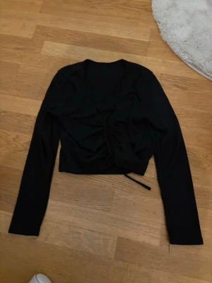 Svart croppad topp med snörning - Snygg svart croppad topp med långa ärmar och snörning framtill som ger en cool detalj. Perfekt till jeans eller kjol för en trendig look. Materialet känns mjukt och stretchigt, vilket gör den bekväm att bära.