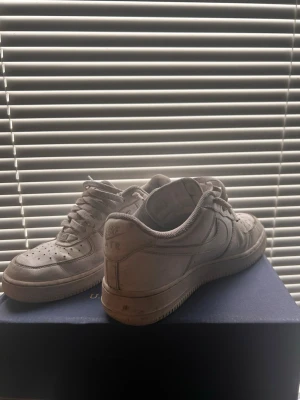 Vita Nike Air Force 1 sneakers - Klassiska vita Nike Air Force 1 sneakers i lågt utförande. Skorna har en stilren design med perforerad tå, tjock sula och Nike-logga på sidan. Tillverkade i läder med vita skosnören och detaljer. Perfekta för dig som gillar streetwear och tidlös stil.