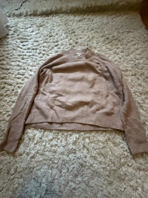 Beige ribbstickad tröja - Mysig beige stickad tröja med rund hals och långa ärmar. Tröjan har en enkel, avslappnad passform och ribbstickade detaljer vid ärmslut och nederkant. Perfekt för lager på lager under kyliga dagar.