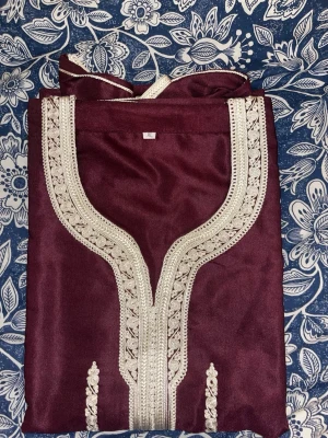 Vinröd kaftan med broderi - Säljer en vinröd kaftan med vackra silvriga broderier längs halsringningen och framtill. Plagget har en traditionell design och är tillverkat i ett glansigt tyg som ger en lyxig känsla. Perfekt för dig som vill sticka ut med något unikt och elegant.
