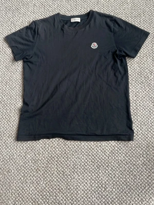 Svart t-shirt från Moncler - Snygg svart t-shirt från Moncler med klassisk rund hals och liten Moncler-logga på bröstet. Tillverkad i mjuk bomull och har en enkel, stilren design som passar till det mesta.