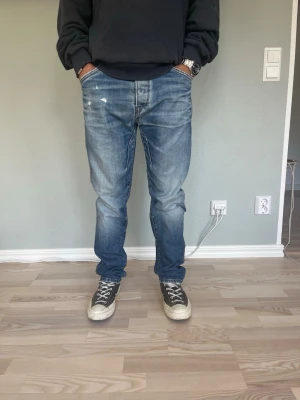 Jack & Jones Originals Erik Anti Fit W31 L32 – Vintage fade | Mörkblå - Storlek: W31 L32 Passform: Anti Fit — avslappnat och generöst sitt utan att vara baggy Färg: Mediumblå med naturlig vintage fade Kollektion: Originals by Jack & Jones  Anti Fit är en av J&J:s mer eftertraktade passformar — rak och avslappnad med lite extra utrymme i lår och höft. Naturlig fading och whiskering som ger dem karaktär.  Modellen på bilden är 175 cm och väger 65 kg — jeansen sitter avslappnat och modernt.  Skick: Bra skick. Små slitningar enligt bild.