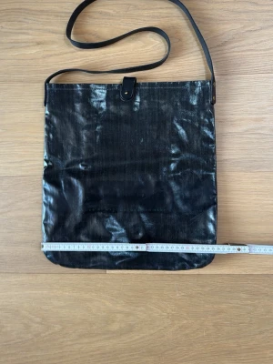 Axelväska  i coatad denim - Köpt i Marc by Marc Jacobs butiken i London runt 2009. Tillhör  ”merch-kollektionen” (BookMarc?) så var inte så dyr i inköp. Snygg mörkblå axelväska med lång rem i svart skinn och enkel knappstängning. Väskan har en rektangulär form och är gjord i en glansigt coatad denim som ger en cool look. Svart board med texten ”Jacobs by Marc Jacobs for Marc by Marc Jacobs” ”in collaboration with Marc Jacobs for Marc by Marc Jacobs” Perfekt för dig som vill ha en stilren och praktisk väska till vardagen.