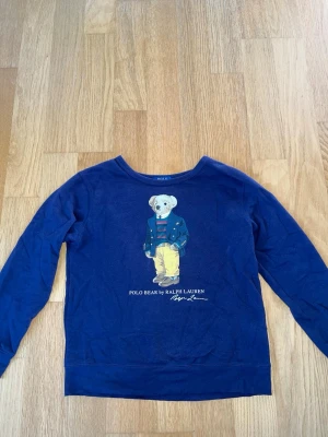 Ralph Lauren polo bear tröja  - Säljer denna marinblå Ralph Lauren sweatshirt i storlek 14-16 år. Tröjan är i bra skick, men eftersom den använts mycket har färgen bleknat lite, annars inga tecken på användning. Nypris på liknande tröjor är mellan 1000-2000 kronor. Hör av er vid funderingar. 