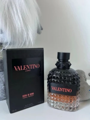 Valentino Uomo Born In Roma Coral Fantasy - Valentino Uomo Born In Roma Coral Fantasy är en parfym i en lyxig glasflaska med nitar och svart lock. Flaskan har en gradient från svart till transparent med korallfärgad vätska. Förpackningen är svart med rosa text och rymmer 100 ml.