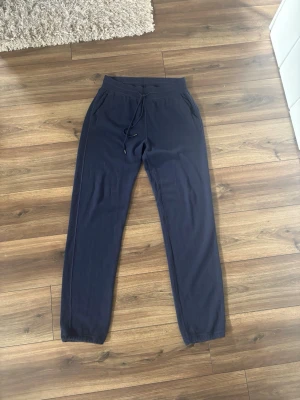 Mörkblå mjukisbyxor från Loro Piana - Exklusiva mörkblå mjukisbyxor från Loro Piana i 100% baby cashmere. Byxorna har dragsko i midjan, två sidofickor och muddar vid bensluten. Perfekta för dig som vill ha både stil och komfort i vardagen. Nypris 21,000kr. Galge tillkommer. Passar en M/L