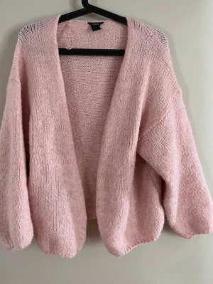  Slutsåld Lindex Ljusrosa oversized stickad kofta - Mysig ljusrosa stickad kofta med oversized passform och ballongärmar. Koftan har öppen front utan knappar och är gjord i ett mjukt, fluffigt material som känns skönt mot huden. Perfekt att slänga över en t-shirt eller topp för en avslappnad look.