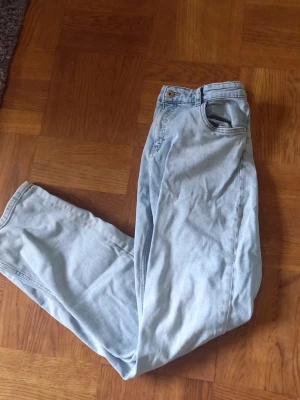 Ljusblå raka jeans - Säljer ett par ljusblå jeans med rak passform och klassisk femficksdesign. Jeansen har normal midja och stängs med knapp och dragkedja. Perfekta för en avslappnad och trendig look. Materialet är denim i bomull.