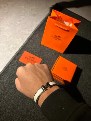 Hermès armband - Snyggt vitt armband från Hermès med silverfärgat H-spänne. Armbandet har en stilren och modern design med en blank finish och är tillverkat i metall och emalj. Perfekt accessoar för att lyfta din outfit.