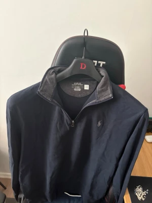 Mörkblå quarter-zip från Polo Ralph Lauren - Snygg mörkblå quarter-zip tröja från Polo Ralph Lauren med klassisk broderad logga på bröstet. Tröjan har hög krage med dragkedja och är tillverkad i mjuk bomullsblandning. Perfekt för en stilren och avslappnad look.