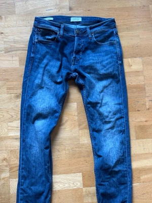 Mörkblå slim fit Jack and Jones jeans - Säljer ett par mörkblå jeans med raka ben och klassisk femficksmodell. Jeansen har snygga slitningar framtill och kontrastsömmar. Materialet är denim i bomull och passformen är normal. Perfekta till en avslappnad stil.