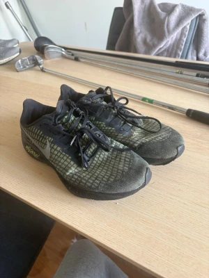 Nike svarta och gröna jigging skor - Nike sneakers med svart och grönt rutmönster på ovandelen, svarta snören och sula. Swoosh-logga på sidan och texten 'Nike Zoom' på hälen. Ovandelen är i meshmaterial för bra andningsförmåga och skon har en sportig, låg profil. Jigging skor