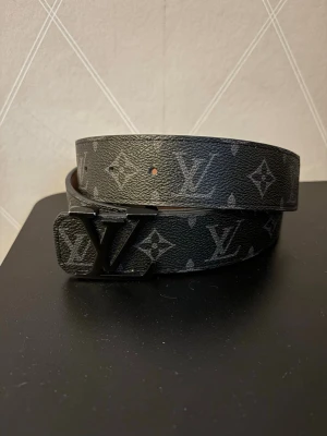 Elegant designerbälte med monogram - Elegant designerbälte med klassiskt monogrammönster. Bältet är tillverkat av högkvalitativt läder och är perfekt för att ge vilken outfit som helst en touch av lyx. Justerbar passform för god komfort.