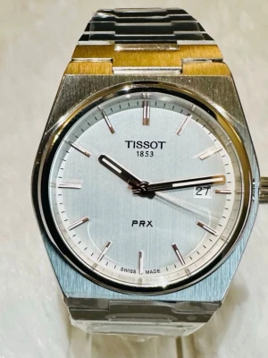Tissot PRX silverfärgad klocka - Stilren Tissot PRX klocka i silver med metallarmband och rund urtavla. Urtavlan är ljus med minimalistiska markeringar och datumfönster vid kl 3. Klassisk design som passar till många stilar. Boetten har borstade och polerade detaljer.