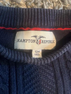 Mörkblå kabelstickad tröja Hampton Republic - Säljer en mörkblå kabelstickad tröja från Hampton Republic i storlek 134/140. Tröjan har rund hals, ribbstickade muddar och ett klassiskt kabelmönster framtill. Perfekt för dig som gillar stilrena och tidlösa plagg.