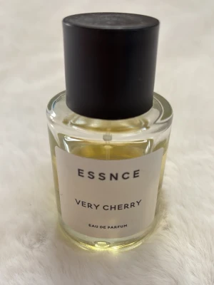 ESSNCE Very Cherry parfym - ESSNCE Very Cherry Eau de Parfum i en rund glasflaska med svart lock. Doften har en fruktig och söt karaktär med tydliga körsbärstoner. Flaskan är genomskinlig och etiketten är vit med svart text.