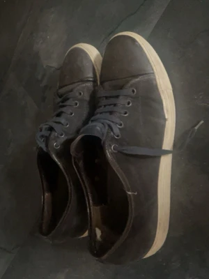  lanvins - Säljer ett par svarta sneakers med lågt skaft och vita sulor. Skorna har svarta skosnören och metallhål för snörningen. Klassisk och enkel design som passar till det mesta. Skick 7,5/10 inget fel på dom alls 