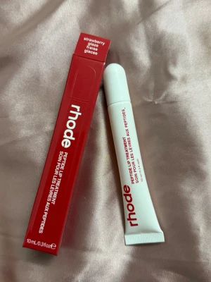 rhode Peptide Lip Treatment Strawberry - Peptide Lip Treatment från rhode i smaken Strawberry Glaze. Tuben är vit med röd text och har en smidig applikator. Förpackningen är röd och matchar smaken. Innehåller 10 ml och är perfekt för att återfukta och vårda läpparna.