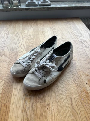 Diesel Sneaker - Snygga vita sneakers med svart detalj på sidan och röd sula. Skorna har klassisk snörning och låg profil. Materialet är textil och syntet, vilket ger en avslappnad och trendig look. Perfekta för dig som gillar streetstyle och enkel design.