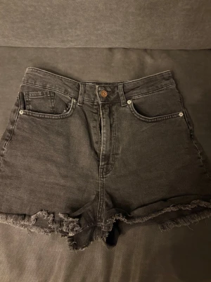 Högmidjade svarta jeansshorts - Säljer ett par högmidjade svarta jeansshorts med råa, fransiga kanter. 