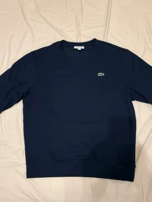Mörkblå sweatshirt från Lacoste Sport - Mörkblå Lacoste Sport sweatshirt i storlek M. Aldrig använd och i mycket fint skick. Klassisk modell med krokodillogga på bröstet.