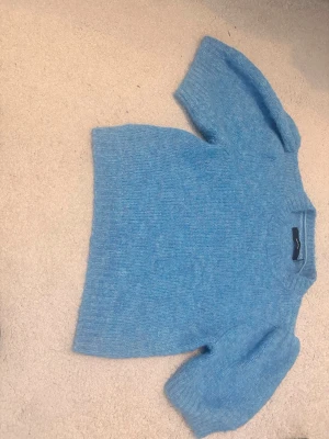 Blå stickad tröja med puffärm - Mysig blå stickad tröja med korta puffärmar och rund halsringning. Tröjan har en mjuk, luddig struktur och ribbstickade detaljer vid ärmslut och nederkant. Perfekt för dig som gillar en avslappnad men trendig stil.