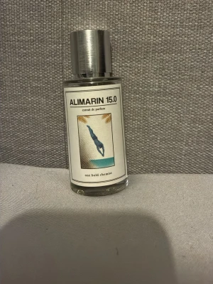 Alimarin 15.0 parfymflaska - Säljer en stilren parfymflaska med namnet Alimarin 15.0 från One Bold Chemist. Flaskan är genomskinlig med metallfärgat lock och har en etikett med en illustration av en dykare. Innehållet är ljusgult och flaskan är i glas.