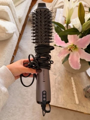Remington varmluftsborste grå - Säljer en grå varmluftsborste från Remington med rund borste och svarta borststrån. Handtaget har knappar för olika inställningar och en lång sladd. Perfekt för att styla håret och skapa volym.