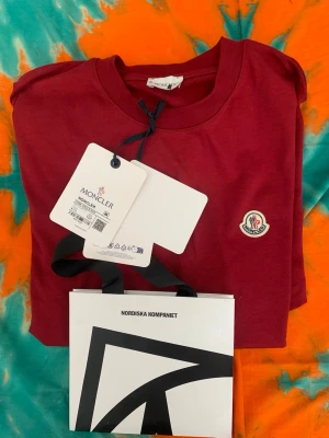 Vinröd Moncler t-shirt i bomull - Snygg vinröd t-shirt från Moncler i mjuk bomull. Klassisk passform med rund hals och Moncler-logga på bröstet. Perfekt till jeans eller shorts för en clean och stilren look.