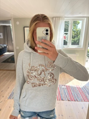 Superdry hoodie - Superdry hoodie i mycket fint skick med den klassiska Superdry-loggan i roséguldpaljetter.  Märkt EU 42 (XL), men jag skulle säga att den passar mer som en L. Se gärna bilderna för passform.  Mjuk, skön och lätt att matcha till både jeans, shorts och leggings.  📏 Märkt storlek: EU 42 (XL) 📐 Upplevd passform: L ✨ Skick: Mycket bra