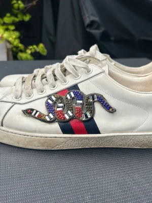 Gucci ace snake  - Säljer nu mina feta och sällsynta Gucci ace. Dem är traditionella snake designen fast med kristaller istället för typ( dem glittrar inte) dem är använda och det finns tydligt täcken på slitage, sömmarna har gått upp vid tån på skon, men det är inget som påverkar skon och det är väldigt lätt att fixa hos en skomakare 