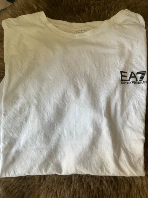 Vit EA7 Emporio Armani t-shirt -  vit t-shirt från EA7 Emporio Armani med diskret logga på bröstet. Klassisk rund halsringning och korta ärmar. 