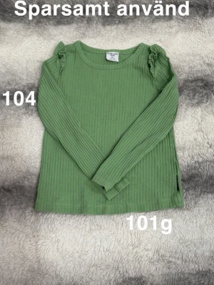 Grön ribbad långärmad topp - Snygg grön ribbad topp med långa ärmar och diskreta volangdetaljer vid axlarna. Perfekt för dig som gillar en enkel men trendig stil. 🌸 Sparsamt använd. Storlek 104