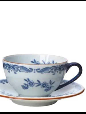 Blåvit tekopp med fat - Säljer 2 st  klassisk kaffekoppar  med tillhörande fat i porslin från Rörstrand ostindia. . Koppen har ett blått blommönster och en blå kant, samt ett matchande handtag. Fatet har samma mönster och en tunn orange kant. Perfekt för te eller kaffe.