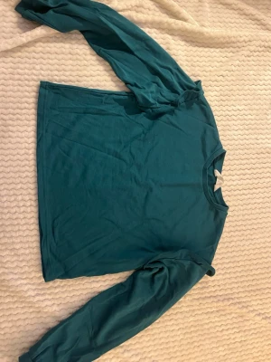 Turkos långärmad tröja - Enkel och stilren turkos långärmad tröja i mjukt material. Tröjan har rund halsringning och raka ärmar, perfekt för en avslappnad look. Passar bra till jeans eller kjol för en chill vardagsstil.