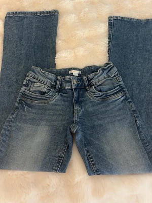 Blå bootcut jeans - Ett par blå bootcut jeans medklassisk femficksmodell. Jeansen har låg midja och svagt utsvängda ben,Tillverkade i denim med snygg tvätt och kontrastsömmar. Perfekta för dig som gillar en avslappnad men trendig stil. Använt 3 gånger så i princip nya inga defekter. 