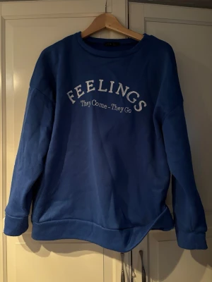 Blå sweatshirt från SHEIN med tryck - Blå sweatshirt från SHEIN i storlek XS med texten 'FEELINGS They Come - They Go' på bröstet. Tröjan har rund halsringning, långa ärmar och mjukt. Är lite nopprig. 