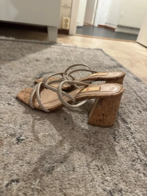 Beige sandaler med korkklack - Snygga sandaler med fyrkantig tå, flätade beige remmar och hög blockklack i korkmaterial. Perfekta för dig som gillar trendiga och stilrena skor med en naturlig touch. Lätta att matcha till olika outfits och ger en cool vibe.