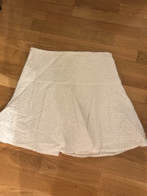 Vit broderad kjol från H&M - Söt vit kjol från H&M i storlek 34. Kjolen har broderade hålmönster och är fodrad för extra komfort. Den har en lätt utsvängd form och passar perfekt till sommaren. Materialet känns luftigt och mjukt.