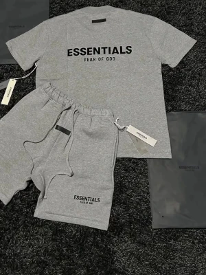 Grå pyjamas-set från Essentials - Snyggt grått pyjamas-set från Essentials Fear of God med t-shirt och shorts. Båda delarna har svart logotyptryck framtill. T-shirten har rund hals och korta ärmar, shortsen har resårmidja och dragsko. Perfekt för chill hemma eller som loungewear.