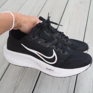 Svarta Nike sneakers med vit sula - Snygga svarta Nike sneakers med vit sula och tydlig vit swoosh på sidan. Ovandelen är i mesh för bra andningsförmåga och skorna har svarta skosnören. Sulan är märkt med 'ComfiRide' för extra komfort. Perfekta för en sportig och trendig look. Använda ett fåtal gånger då sonen har flera skor att välja på. Säljs då dom tyvärr nu är för små.  Innermått 25,5cm