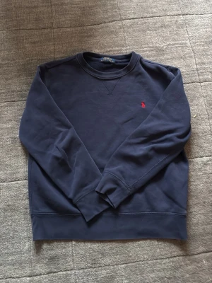 Mörkblå sweatshirt från Polo Ralph Lauren - Ralph lauren tröja i storlek 10-12. Passar från 145-158 cm. Sparsamt använd. Hör av dig vid minsta fundering! Liten defekt på armen 