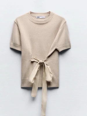 Beige stickad topp med knytband - Trendig beige stickad topp från Zara med korta ärmar och rund halsringning. Toppen har ett dekorativt knytband i midjan som ger en snygg siluett. Perfekt att styla med jeans eller kjol för en avslappnad look. Passar som s-m. Säljer eftersom den är för smal för mig!