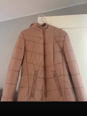 Beige pufferjacka med huva - Superfin jacka från Bershka! Säljer en beige pufferjacka med huva och dragkedja framtill. Jackan har två snedställda fickor med dragkedja och quiltad design. Perfekt för kalla dagar och riktigt skön att bära. Materialet är syntet och jackan har en modern, enkel look.