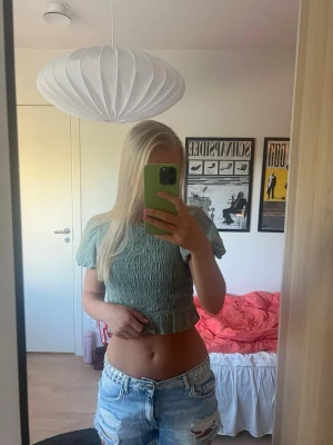 Grön smockad topp med puffärm - Ljusgrön topp med smockad passform och volangkant nedtill💚 Toppen har ascoola puffärmar och en rund halsringning samt knappdetalj bak. Jättefin som festtopp eller sommartopp! Materialet är polyester.