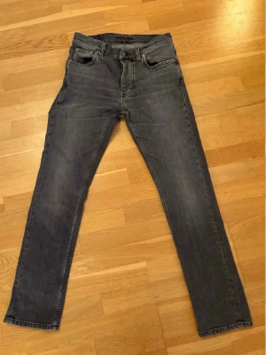 Nudie jeans grim tim w29 l30 - Säljer ett par grå slim fit jeans med klassisk femficksdesign och svarta sömmar på bakfickorna. Jeansen har normal midja och raka ben, perfekta till vardagslooken. Materialet är mjukt och stretchigt jeans för skön passform.