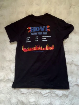Svart Hov1 tour t-shirt med flames - Svart t-shirt med Hov1 4-Ever Tour 2024-tryck på ryggen och eldflames i färg. Framtill finns en liten blå krona. 