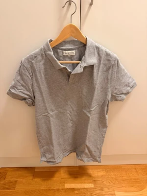 Grå studio total piké tröja medium - Klassisk grå pikétröja från studio total med krage och korta ärmar. Tillverkad i mjuk bomull som känns skön mot huden. Perfekt till jeans eller shorts för en enkel och clean look.Grå studio total piké tröja medium Använd några gånger