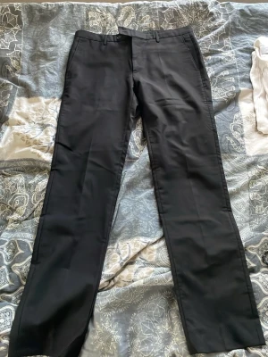 Svarta raka kostymbyxor - Snygga svarta kostymbyxor med raka ben och klassisk passform. Byxorna har hällor för bälte, sidofickor och pressveck framtill. Perfekta för en stilren look och passar till skjorta eller t-shirt.