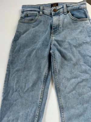 Ljusblå Lee jeans - Säljer ett par klassiska ljusblå jeans från Lee med raka ben och femficksmodell. Jeansen har normal midja, bälteshällor och Lee-logga på bakfickan. Tillverkade i mjuk denim som ger en avslappnad look. Perfekta till sneakers eller boots.